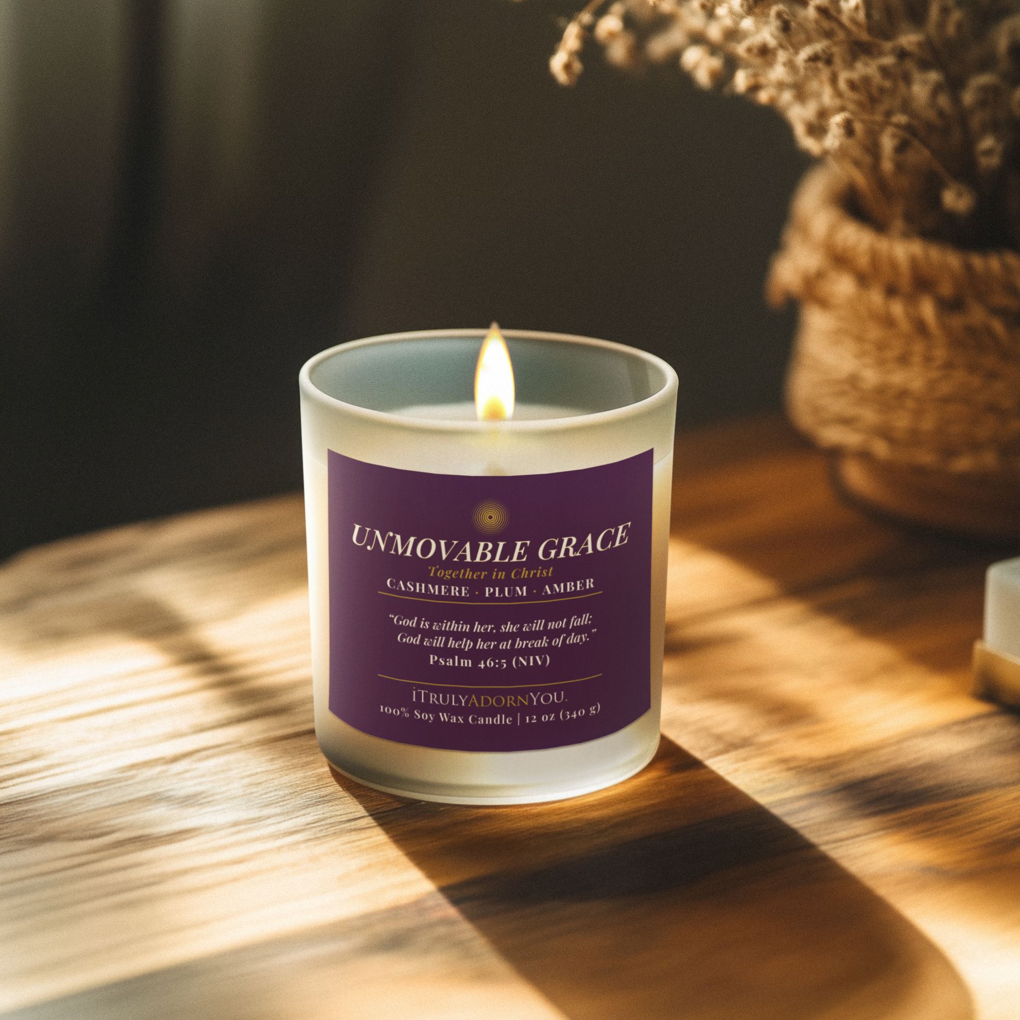 Unmovable Grace candle with a plum purple label on a wooden surface with a blurred background